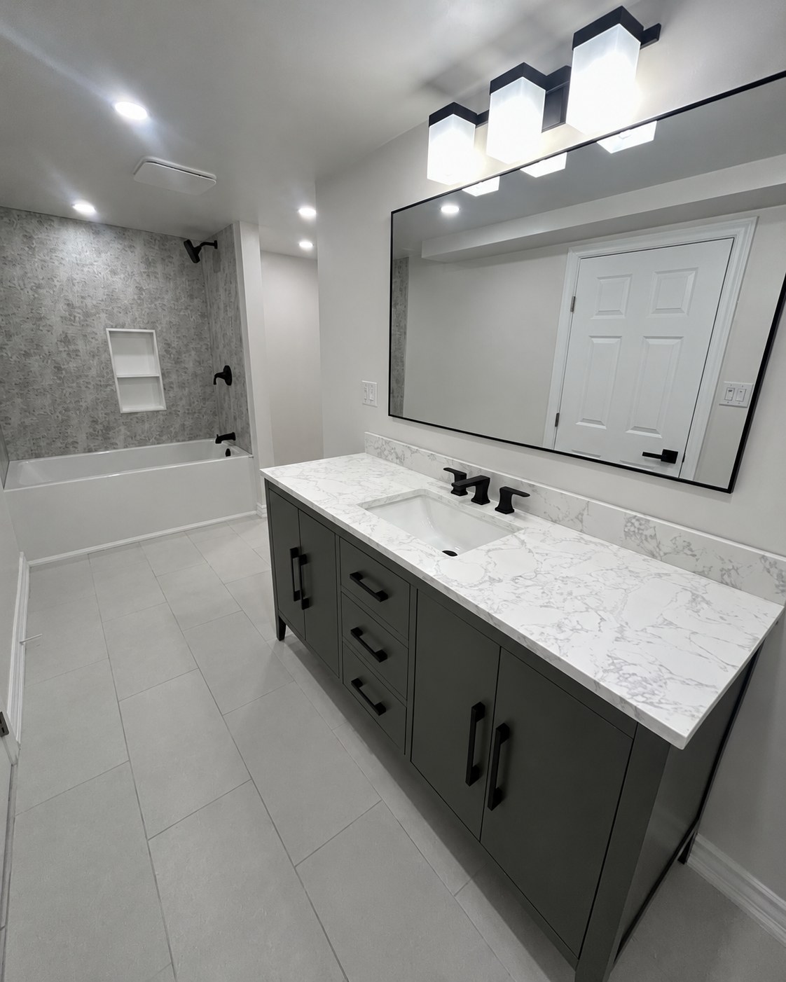 Dark vanity, wide mirror and tiled bathtub surround.