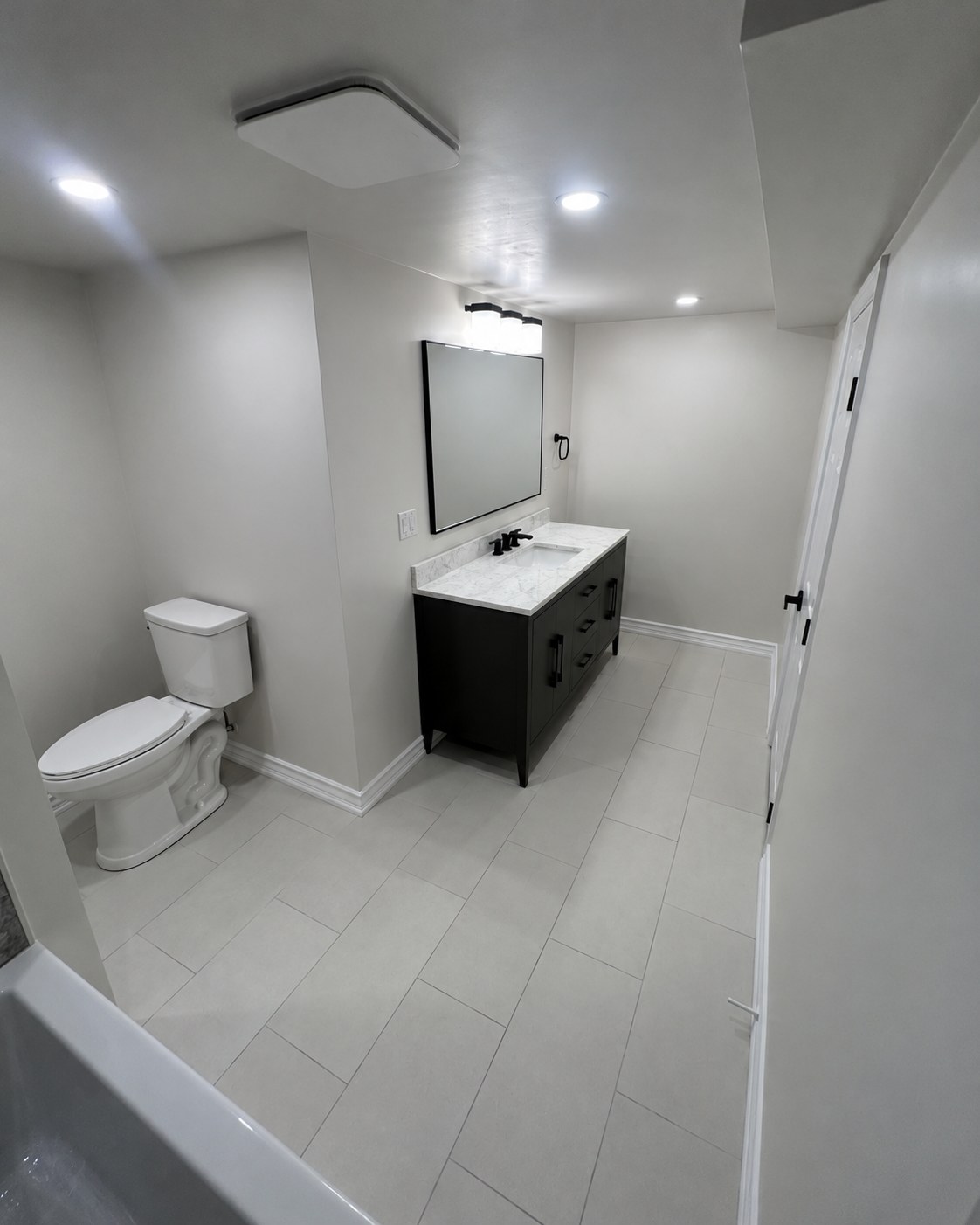 Bathroom with a dark vanity, white fixtures and recessed lighting.