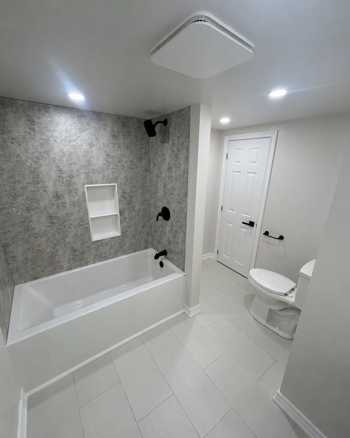 Bathtub with patterned tile, a recessed shelf and black fixtures.