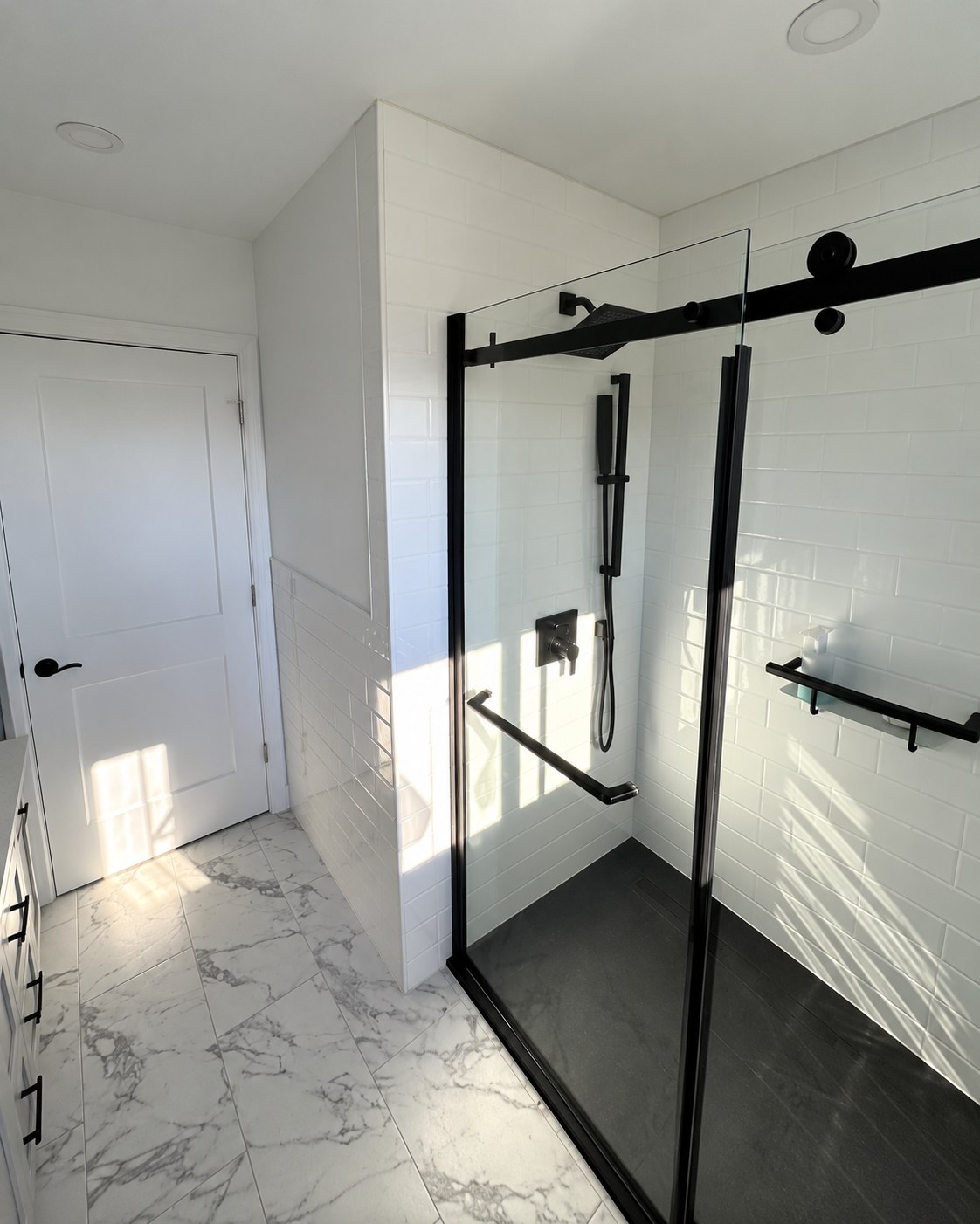 Glass shower with black hardware and marble-look floor tile.