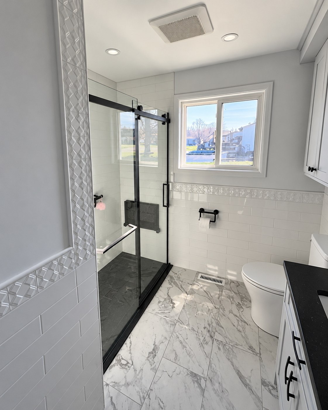 Glass shower enclosure beside a vanity and window.